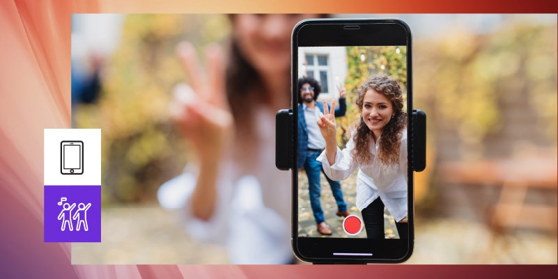 Na imagem, uma homem e uma mulher descobrem como postar vídeos no TikTok na frente de um celular na vertical, conectado a um suporte.