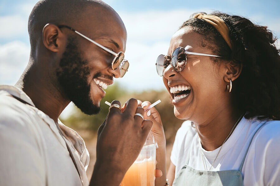 A imagem mostra duas pessoas se divertindo em um encontro de casal. Eles compartilham uma bebida e usam óculos escuros.