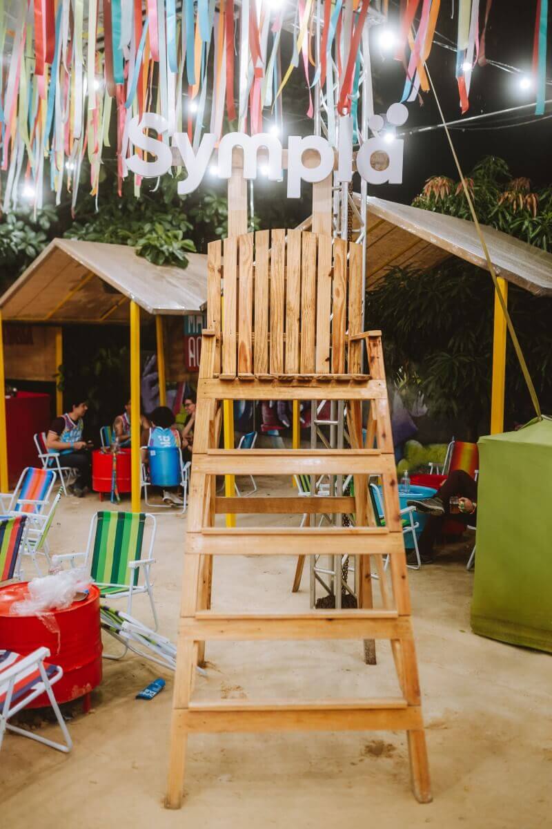 Espaço instagramável com uma cadeira de salva-vidas e o letreiro 'Sympla' na decoração de uma festa de Carnaval.