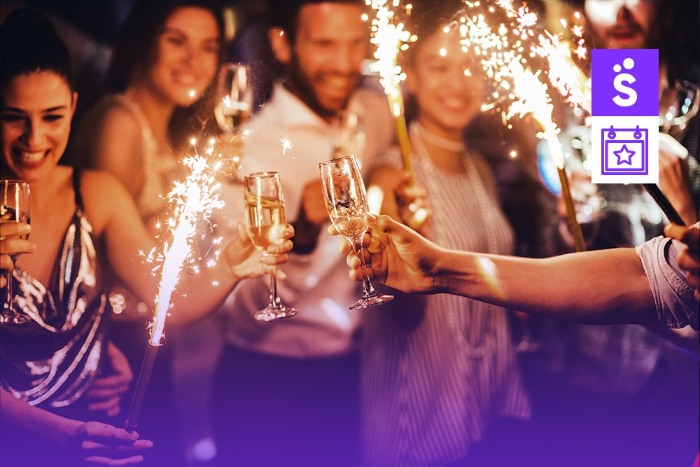 Cinco pessoas celebrando o fim de ano com taças de champanhe e fogos de artifício.